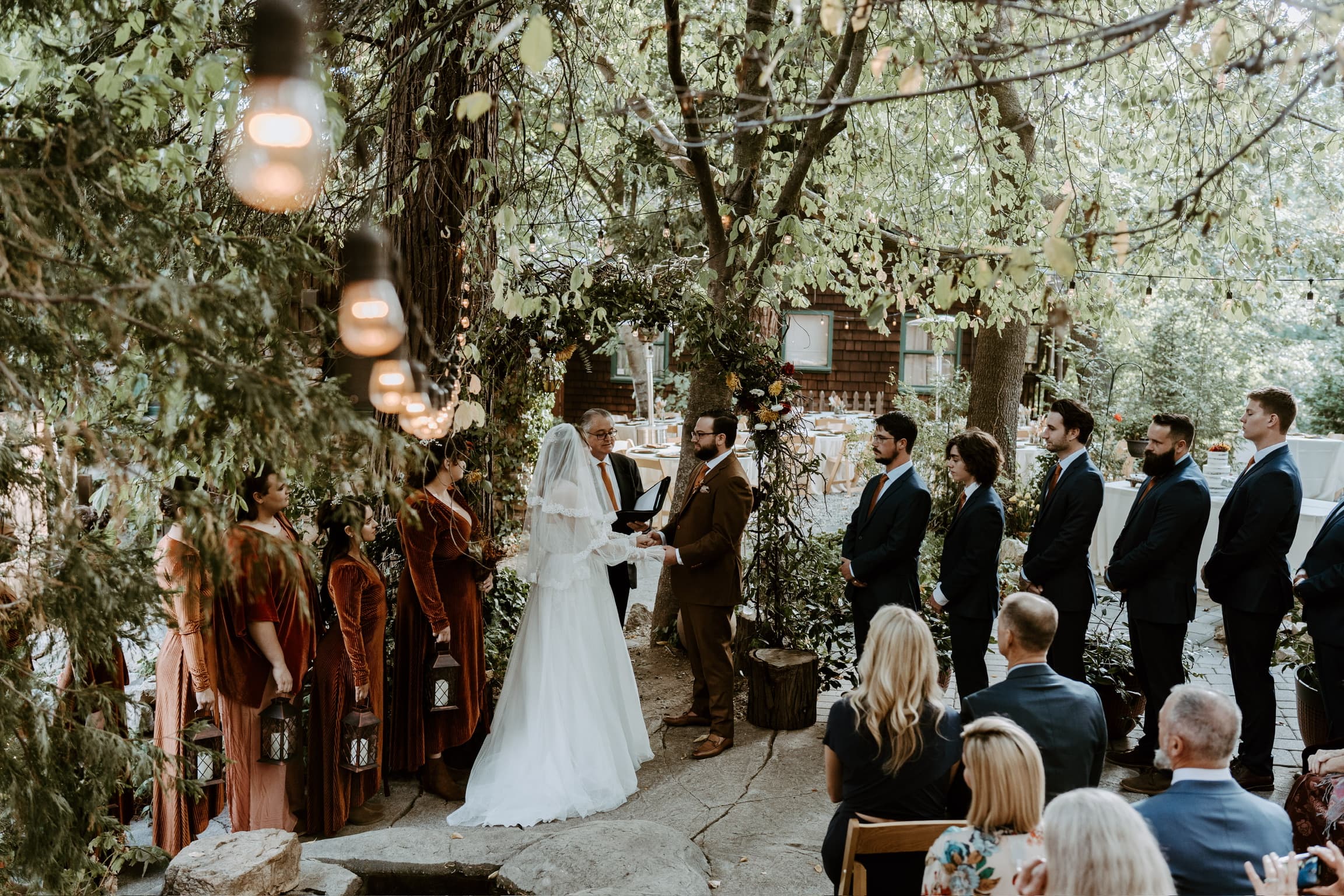 A couple exchanging vows in front of seated guests beneath the pines at Willow Woods Park
